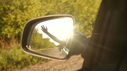 Happy travel woman enjoy freedom summer road trip with hand in window back mirror reflection view. Smiling female tourist in driving automobile exploration adventure bright sun light with green trees
