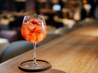 Transparent pink alcohol cocktail in wine glass with ice, aperol and gin on bar counter in...