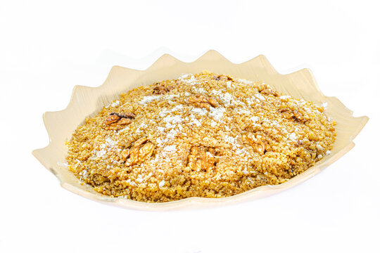 Rfiss: Algerian traditional semolina-based dessert, enriched with dried fruit and whole nuts, sprinkled with powdered sugar. Served on a decorative plate, side view isolated on a white background