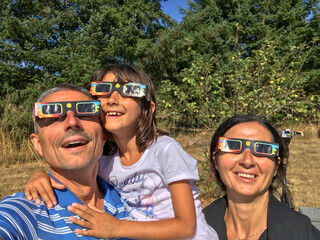 Mother, father and daughter looking at the sun during a solar eclipse on a country park, family...