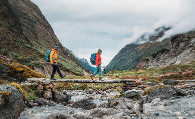 Trekkers Couple crossing river by wooden bridge on Mera Peak trekking route near Kothe. Man and woman returning down to valley and enjoying Makalu Barun National Park valley view.