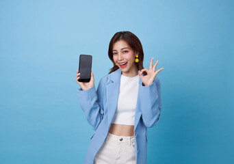 Beautiful Asian teen woman holding smartphone mockup of blank screen and shows ok sign isolated on...