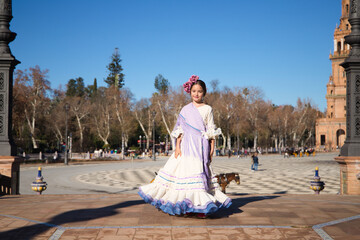 a little girl dancing flamenco dressed in a beige dress with ruffles and purple fringes in a famous...