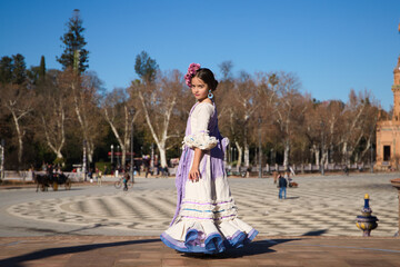 a little girl dancing flamenco dressed in a beige dress with ruffles and purple fringes in a famous...