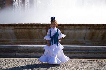 A pretty little girl dancing flamenco dressed in a white dress with ruffles and blue fringes in a...