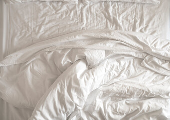 Morning time, messy, crumpled used white blanket on a bed, top view.
