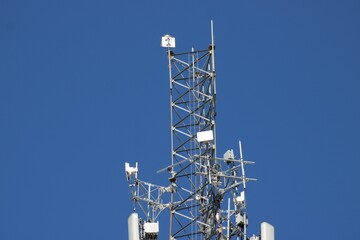 A three-tier cell tower is once again having additions made to the already high tower that must be climbed via  foot spikes or ladders. 