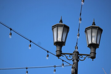Stings of lights anchored by twin lamp post in a town's green space that bridges the past and the...