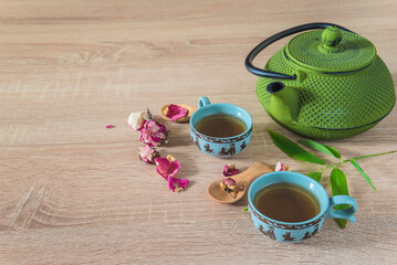 Chinese tea time concept: two chinese cups of tea, green teapot and petal of roses on a wooden background