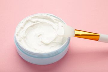 Cosmetic mask (scrub) in a bowl with brush on pink background.