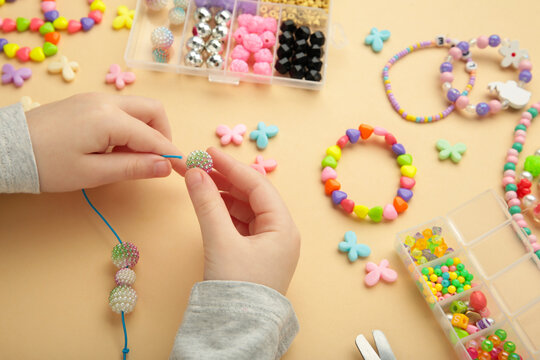 Little girl made bracelets on beige background. Kids handmade beaded jewelry. DIY bracelet beads.