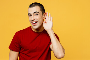 Young curious nosy fun middle eastern man he wear red t-shirt casual clothes try to hear you overhear listening intently isolated on plain yellow orange background studio portrait. Lifestyle concept. - obrazy, fototapety, plakaty