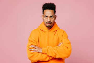 Young sad man of African American ethnicity wears yellow hoody casual clothes hold hands crossed folded look camera isolated on plain pastel light pink background studio portrait. Lifestyle concept.