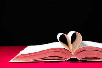 The pages of the book are folded in the shape of a heart on a pink and black background, place for text