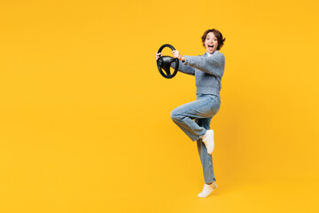 Fototapeta na wymiar Full body side view surprised young woman she wearing grey knitted sweater shirt casual clothes hold steering wheel driving car isolated on plain yellow background studio portrait. Lifestyle concept.