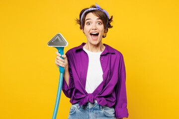 Young shocked surprised woman wears purple shirt casual clothes do housework tidy up hold in hand steamer look camera isolated on plain yellow color background studio portrait. Housekeeping concept. - obrazy, fototapety, plakaty