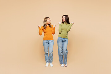 Full body young friends two women they wear orange green shirt casual clothes together do winner gesture celebrate clenching fists say yes isolated on plain light beige background. Lifestyle concept.