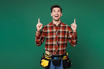 Young employee laborer handyman man wear red shirt point index finger overhead on area isolated on plain green background. Instruments accessories for renovation apartment room. Repair home concept.