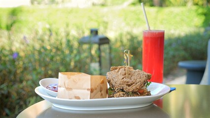 Outdoor dining with fresh sandwich, healthy salad, and refreshing beverage on table with natural bokeh background. Healthy eating and relaxation.