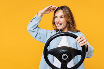 Young smiling happy woman she wear blue shirt white t-shirt casual clothes hold steering wheel driving car look far away distance isolated on plain yellow background studio portrait Lifestyle concept