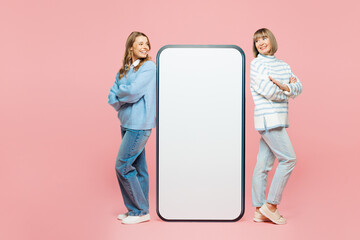Full body elder parent mom young adult daughter two women in blue casual clothes standing big huge blank screen area mobile cell phone smartphone isolated on plain pink background Family day concept