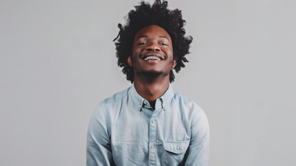 Fototapeta premium cheerful man with curly hair, smiling at the camera, arms crossed, wearing a light blue casual shirt, standing against a light gray background.