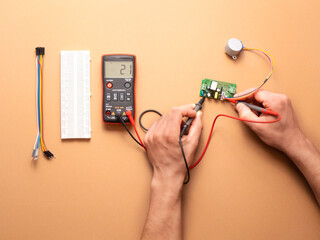Electrician’s hands  with a multimeter on a beige background  - obrazy, fototapety, plakaty