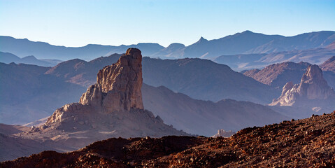 Hoggar landscape in the Sahara desert, Algeria. Steep peaks rise up in a mineral setting - 750081324