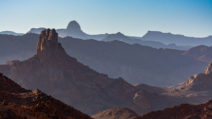 Hoggar landscape in the Sahara desert, Algeria. Steep peaks rise up in a mineral setting - 750081376