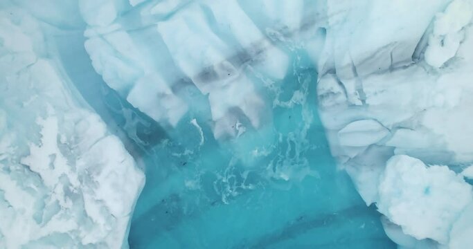 Melting glacier ice washed by ocean waves aerial view. Glacial pattern, ice formation, blue water background. Arctic winter landscape global warming. Climate change and melting icebergs in Antarctica