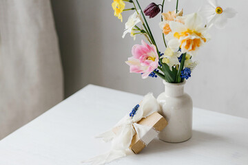 Happy womens day and Mother's day. Stylish gift box with ribbon and spring flowers on rustic white table. Beautiful daffodils and tulips gentle bouquet and present. Space for text