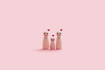 Happy wooden lesbian family figures isolated on a pink background. Two pride moms and smiling kid stand close together