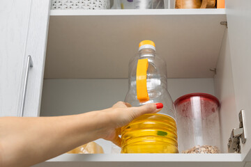  the housewife takes out a bottle of sunflower oil from the kitchen cabinet.