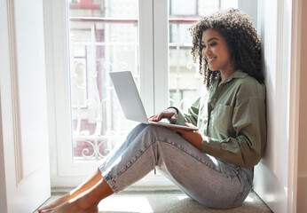 Smiling black woman works and studies on laptop from home - obrazy, fototapety, plakaty