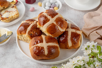 Traditional Easter hot cross buns on a white plate with butter, berry jam and cup of tea. Delicious Easter breakfast.