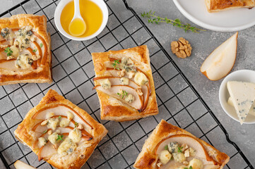 Mini tarts with puff pastry, pieces of pear, blue cheese, walnuts and honey on a concrete background. Top view. - obrazy, fototapety, plakaty