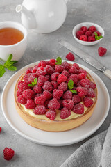 Delicious raspberry tart with vanilla custard cream sprinkled with powdered sugar on a white plate on a gray concrete background. Summer dessert.