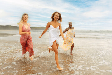 multiracial group of three female friends (latina, white and black) running together along the seashore on a beach on a summer day. summer traveling with friends