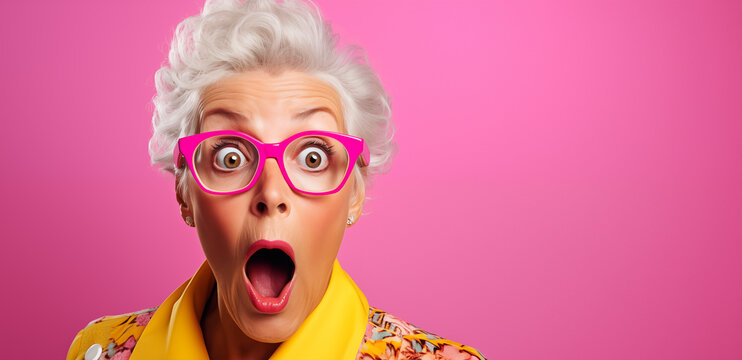 Portrait d'une femme senior surprise, étonnée, portant des lunettes, sur fond rose, image avec espace pour texte.
