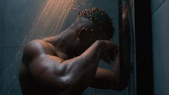 African American muscular strong guy naked wet male sad frustrated man take shower under falling water washing body routine in bathroom suffer depression stress impotence mental psychological tension
