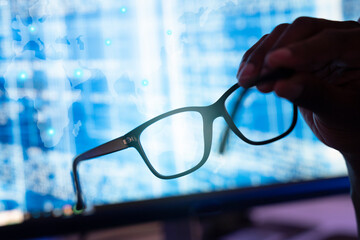 Man's hand holding glasses. background with blue computer screen