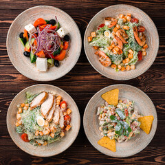Set of chicken and shrimp Caesar salad, Greek salad and vegetable salad on a wooden table.