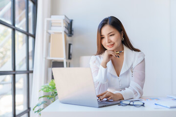 Cheerful asian businesswoman work diligently on her laptop in modern office.