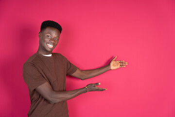 Happy smiling, attractive young black man showing copyspace, on carmin red background. Advertising concept.