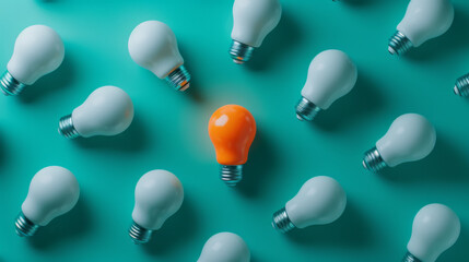 An orange lightbulb glowing among a group of white lightbulbs on a teal background, representing a unique idea or solution.