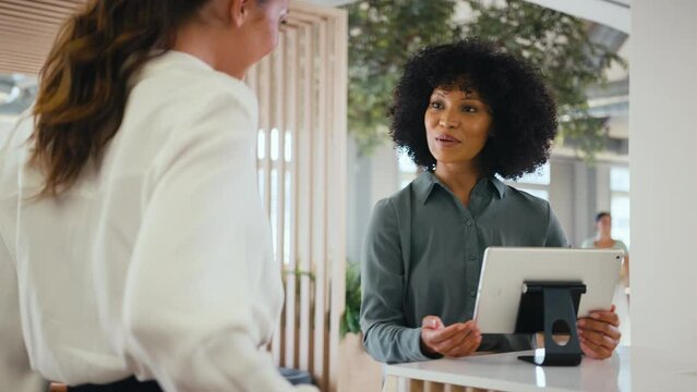 Businesswoman with suitcase checking in at hotel reception for conference - shot in slow motion