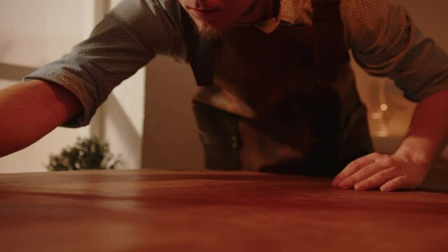 Craftsman looking at piece of genuine leather on table in artisan workshop. Shoemaker working with leather before sewing handmade shoes.