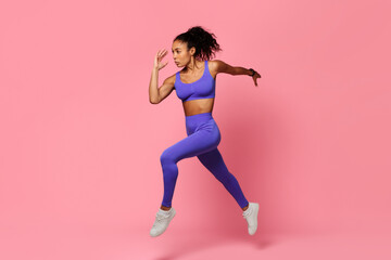 Fototapeta na wymiar Motivated black sportswoman leaps and runs in mid air, studio