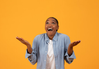 Excited African American woman celebrates special offer over orange backdrop