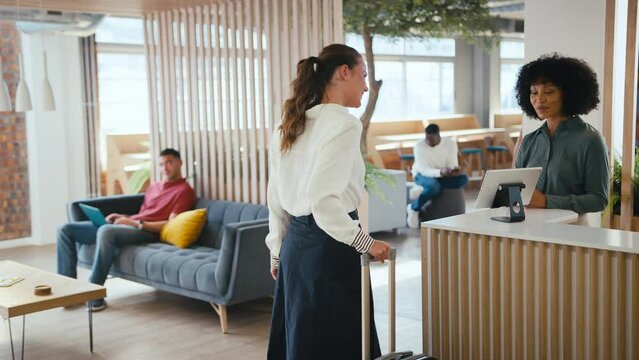 Businesswoman with suitcase checking in at hotel reception for conference - shot in slow motion